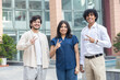 © GAJENDRRA BHATI  - Three young confident indian gen z employees or entrepreneurs businesspeople standing outdoor do victory sign, Teamwork. Success. Happy successful office colleagues achievement.