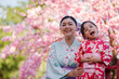 © geargodz - woman and child girl in yukata (kimono dress) on red bridge with sakura flower or cherry blossom blooming in garden