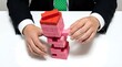 © ALAUDDIN - Businessman carefully removes block from unstable tower, symbolizing business risk and strategy.