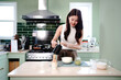 © Stella 16 - Young asian woman preparing matcha tea in a bright modern kitchen, Pouring hot water from a teapot into a cup with matcha powder, preparing traditional Japanese green tea