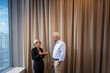 © Johnér - Senior businesswoman communicating with male colleague standing in front of curtain at office