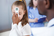 © DC Studio - Close-up shot of an African American doctor using a thermometer to check a young girl fever. The youngster is treated in a hospital room after taking a temperature to get a diagnosis.
