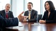 © Nest - Business professionals intently listen to a male colleague actively gesturing during a focused meeting at a polished wooden conference table.