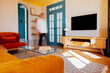 © Dasha Petrenko - Modern living room featuring cozy orange sofa, wooden furniture, and bright blue door, with a person walking through the space, showcasing a stylish interior design concept