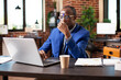 © DC Studio - Pensive male entrepreneur looking at his laptop and tapping forehead with pen, seated at table in brick wall office. African american analyst thinking and concentrating on startup company research.