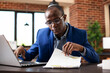 © DC Studio - Black male analyst reading company research information on clipboard and typing on his laptop. African american businessman with spectacles reviewing paperwork at office desk.