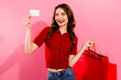 © deagreez - Young stylish woman with red cardigan holding credit card and shopping bags against pink background