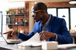 © DC Studio - Focused businessman pointing to device screen and reviewing market analysis documents in startup office. Male analyst sitting at desk with laptop and company paperwork, preparing project presentation.