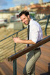 © Teodor Lazarev - Confident businessman leaning on a railing, smiling while checking his mobile phone outdoors, embodying urban connectivity and successful communication