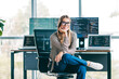© deagreez - Smiling female software developer sitting in modern office with laptops and multiple monitors showing code, relaxed programmer working remotely and enjoying tech-focused creative workspace