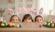 © Konstantin - Curious child girls in bunny ears peeking out from behind table with colorful easter eggs.