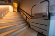 © True Pixel Art - Wide interior stairs rise beside a motorized platform lift with green indicators and fold up arms in Cordoba, Spain, as a staff member crouches near a chalkboard menu.