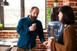 © DC Studio - Businessman and woman share conversation near water cooler in brick wall workspace. Male and female employees hold coffee cups combining casual interaction with productive talk in startup office.