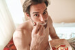 © Teodor Lazarev - Shirtless man enjoying a healthy breakfast of oatmeal with fresh strawberries and banana in bed during a bright morning, promoting wellness and self-care