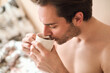 © Teodor Lazarev - Man relaxing in bed and waking up with first morning coffee, starting the daily ritual and enjoying breakfast beverage, shirtless and feeling refreshed