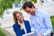 © Teodor Lazarev - Professionals working together outdoors, a smiling woman talking on her smartphone while a happy man is looking at a document, collaborating and communicating in business