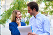 © Teodor Lazarev - Business colleagues collaborating outdoors, a woman having a phone conversation while a man reviews documents, sharing a happy, professional moment in the city