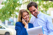 © Teodor Lazarev - Business colleagues collaborating outdoors, a smiling woman talking on her smartphone while a man reviews documents, teamwork and effective communication between partners