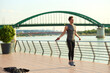 © Teodor Lazarev - Male athlete skipping rope for fitness and cardio workout on a riverside pier with a green arch bridge spanning the river in a city during daylight