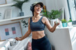 © nenetus - Sporty woman eating yogurt while dancing and listening to music with headphones at home