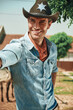© Teodor Lazarev - Smiling man wearing a cowboy hat with sheriff star and denim shirt, portraying a happy western lifestyle at a ranch, looking away at sunlight