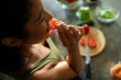 © Marko Geber - Young woman eating tomato slice in home kitchen