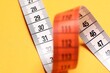 © New Africa - One measuring tape on orange background, above view