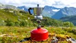 © Ucup - A stovetop espresso maker sits on a portable gas stove outdoors. Lush green vegetation and distant mountains form the backdrop