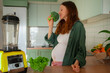 © wifesun - Pregnant woman carefully smelling fresh broccoli, focusing on a healthy diet and nutrition during pregnancy, standing in a modern kitchen with a blender, preparing a wholesome meal