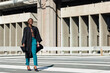 © wavebreak3 - African American woman walking on zebra crosswalk at campus, wearing gown, holding cap, copy space