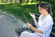 © SISMIZ - Woman having a video call on a tablet while sitting on a park bench with a salad