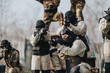 © qunica.com - A group of players in camouflage and masks aim paintball markers in a tactical outdoor drill. They crouch and stand ready, portraying focus and teamwork on the field.