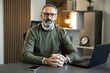 © Dejan - Mature businessman working, sitting at desk with laptop and smartphone, looking at camera in a modern office setup