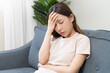 © KMPZZZ - Depressed anxiety asian young woman frustrated hand on head, touching her temples, suffering stressed, sick, tired, crisis on sofa from headache, migraine pain tension problem health care concept.
