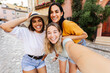 © Xavier Lorenzo - Multiracial young female friends smiling at camera outdoors. Cheerful women posing together during a summer city break. Friendship and lifestyle concept.