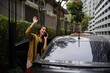 © Parichat - Young Asian woman waving hand while talking on phone and getting out of a car