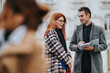 © qunica.com - Two professionals chat outside, one holding a notebook while the other listens. Colleagues share a casual business discussion in an outdoor setting.