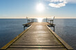 © Volha - A straight wooden pier leads toward open water and a bright sunlit horizon, with simple benches at the end. Minimal coastal scene ideal for relaxation, contemplation, travel, freedom and peaceful seas