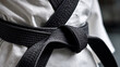 © Oksana - Close up of tied black belt on karate gi, showcasing the texture and details of the fabric, with a clean and minimal background emphasizing the martial arts uniform