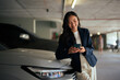 © Parichat - Asian businesswoman smiling using a smartphone in a parking garage