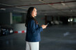 © Parichat - Young Asian woman holding smartphone in parking garage