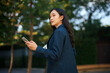 © Parichat - Young Asian woman walking outdoors holding phone thinking