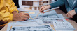 © InfiniteFlow - Hands engaged in architectural design with blueprints and scale models in a collaborative workspace, showcasing creativity and teamwork in the building process. SACTR