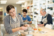 © JackF - Young woman sits at workbench in ceramics workshop, sculpting and shaping clay piece