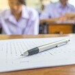 © Lynda Ara - Pen on Exam Paper with Students in Background.
