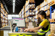 © DC Studio - Asian warehouse clerk printing and preparing sticky tracking numbers tags, managing shipment details and barcodes before delivery. Employee processing orders and managing awb labels.