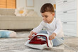 © New Africa - Child safety at home. Little boy playing with iron on floor indoors, space for text