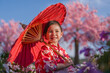 © geargodz - preschool child girl in yukata (kimono dress) holding umbrella with sakura flower or cherry blossom blooming in garden