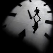 © sornram - A silhouette of a person walking beneath an abstract clock, symbolizing the passage of time and life's hurried moments.