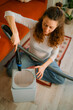 © wifesun - Woman using a vacuum cleaner to meticulously clean the filter of an air purifier on the wooden floor, performing essential household maintenance to promote better hygiene and air quality